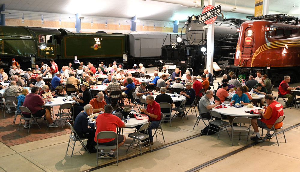 a dozen tables set up with people sitting at them in front of trains - group tours