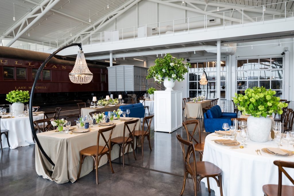Wedding reception with long farmhouse tables, crystal chandeliers, and greenery centerpieces in the Main Floor Exhibit Space at the National Railroad Museum in Green Bay